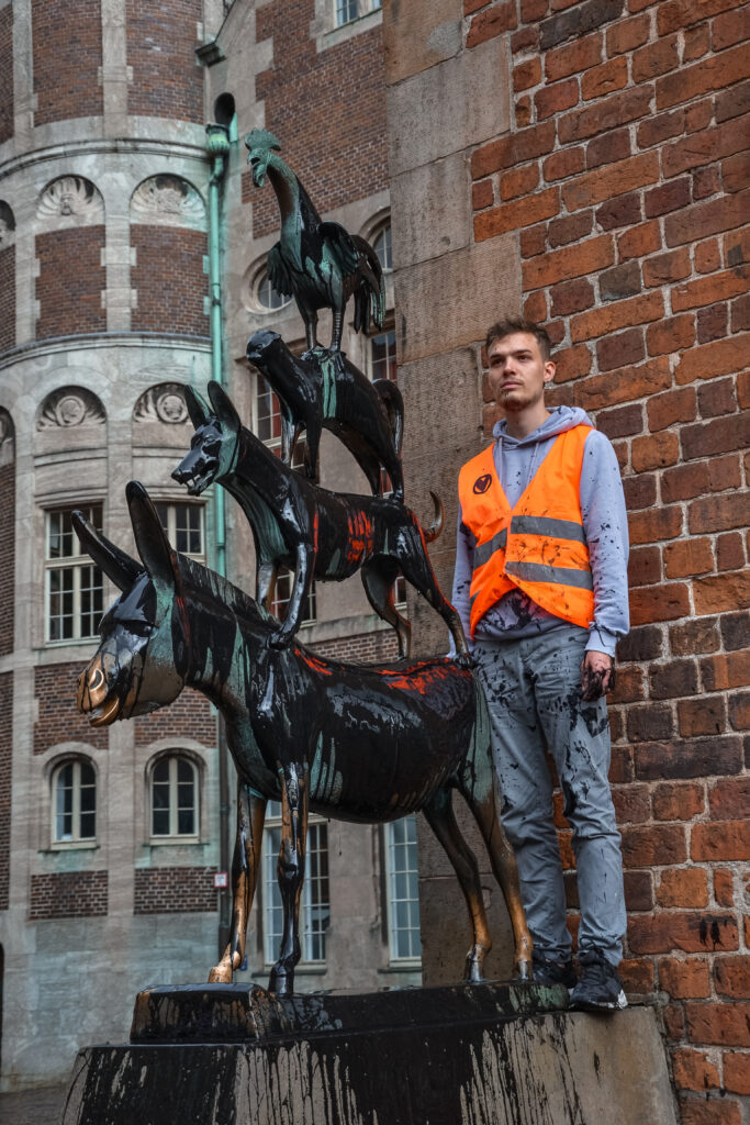 Der Aktivist Fabian Beese von der Letzten Generation steht auf dem Sockel der Bremer Stadtmusikanten